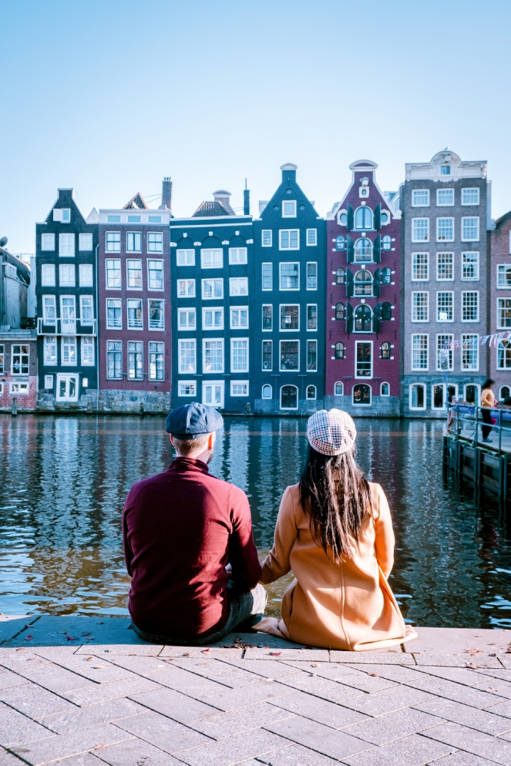 Dos turistas sentados junto a un canal observando la arquitectura de Ámsterdam