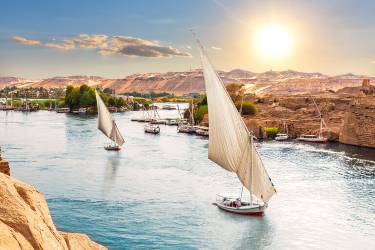 Pequeños barcos de vela surcando las aguas de un río rodeado de montañas pardas